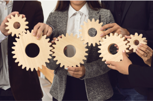 Business professionals holding and interlocking wooden gears together as a symbol of collaboration and working systems.