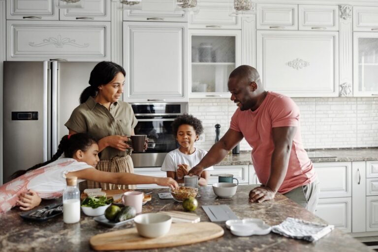 A family of four gathers around a kitchen island for breakfast in a bright, modern kitchen.